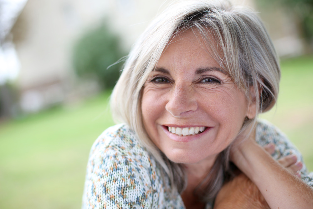 Mature woman smiling while leaning her head on her foldering arm. Nonsurgical skin tightening.