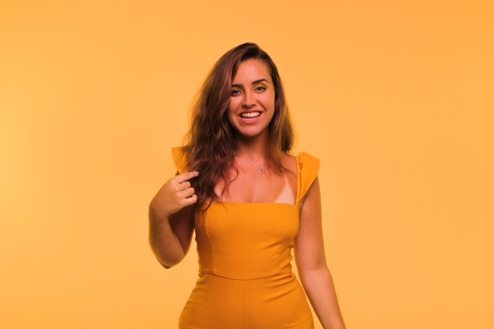Woman in yellow dress playing with her hair and smiling.